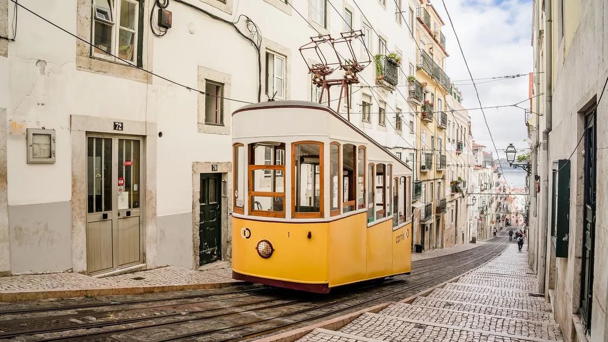 A yellow funicular tram climbing a narrow cobblestone street between whitewashed buildings in Lisbon